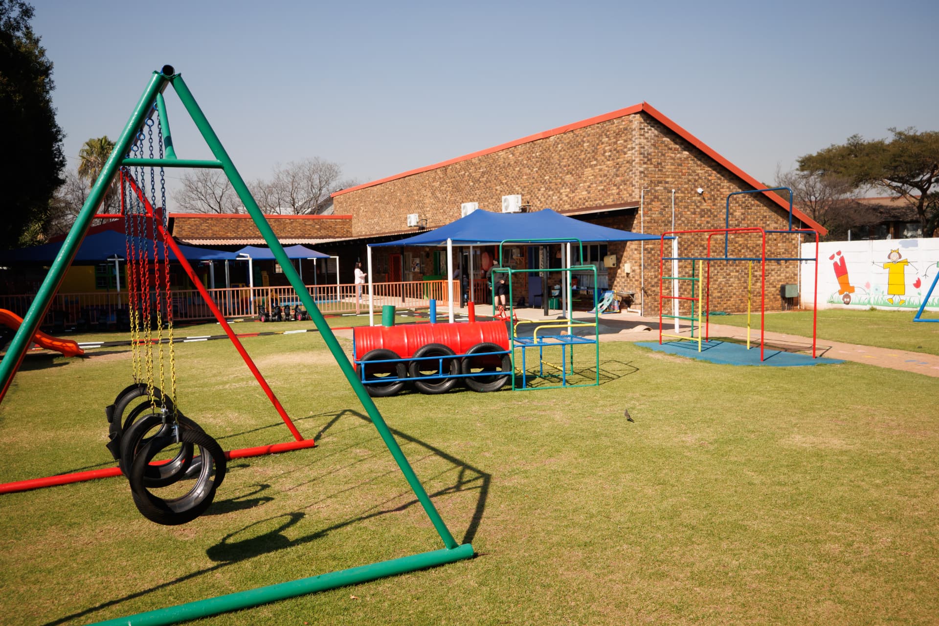 Wide view of the grass field with swings, climbing frames and shade nets
