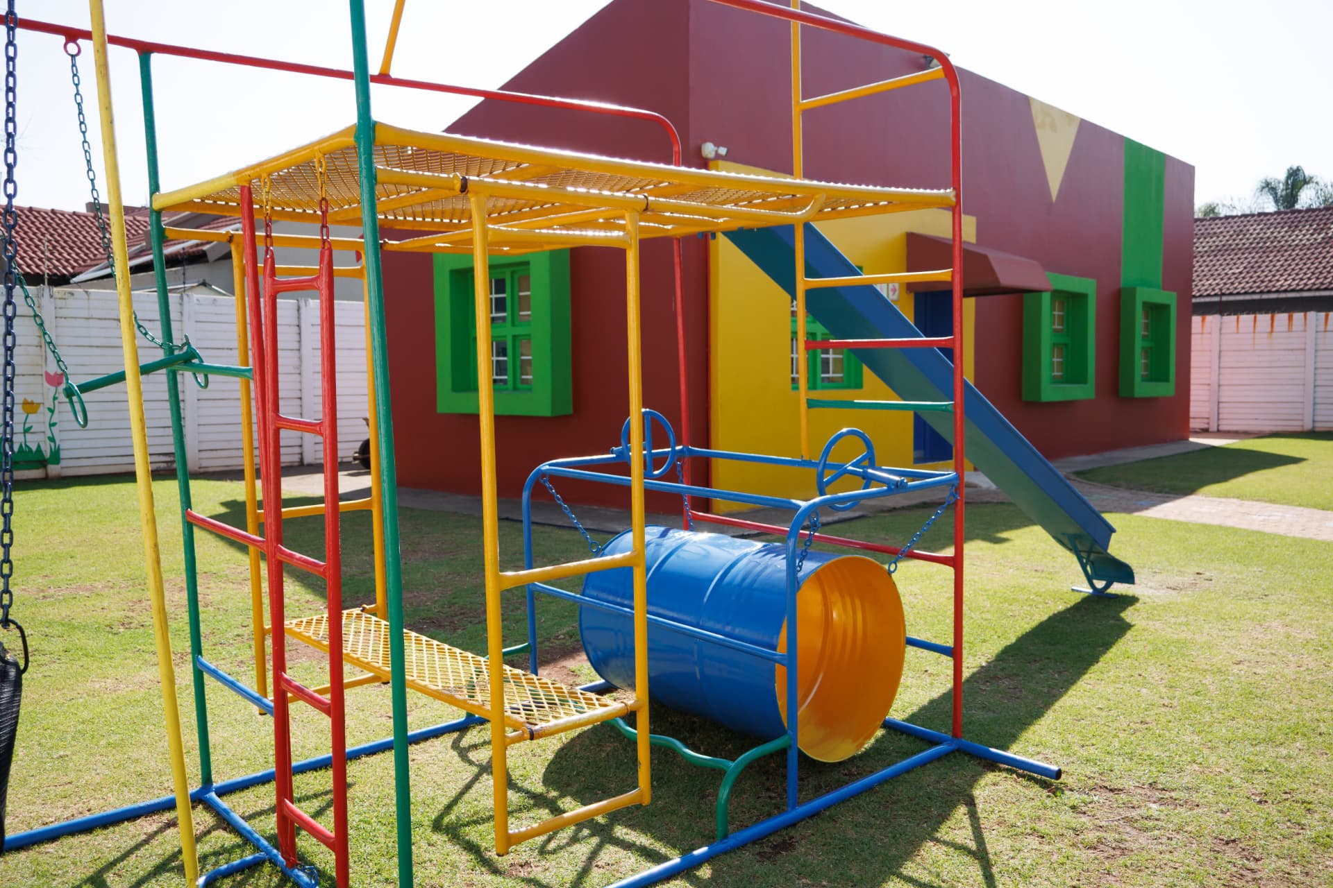 Colourful jungle gym and swings in front of the painted play house